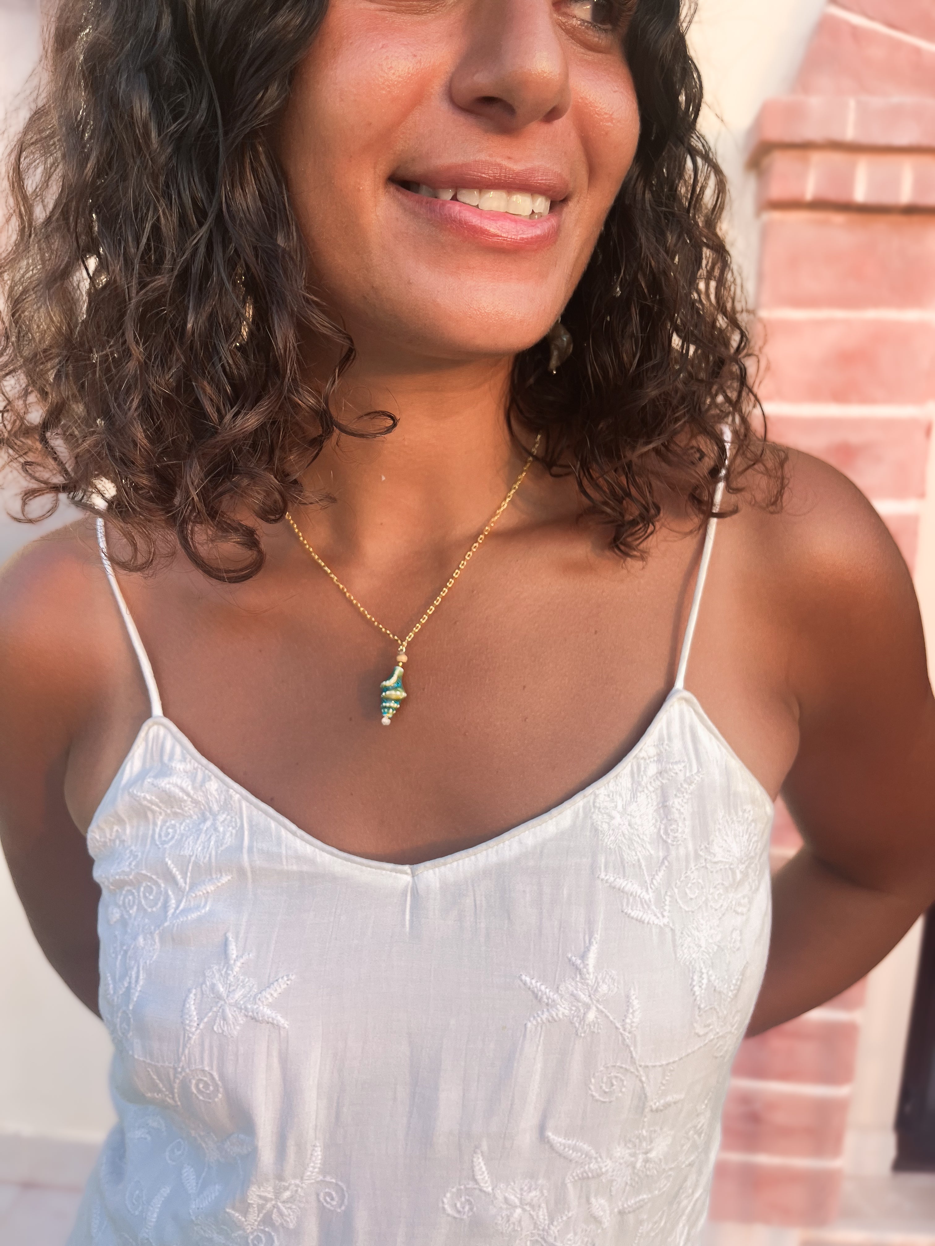 Gold chain necklace with coral and turquoise spiral shell pendant, close-up on model