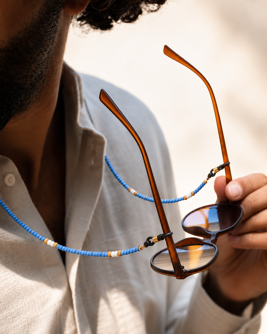 Person holding a pair of sunglasses with a blue beaded chain 