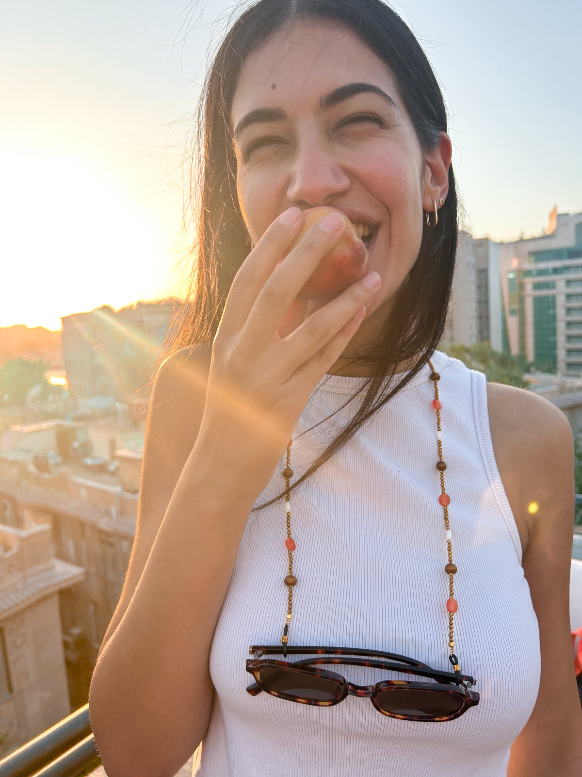 A close up shot of a woman wearing a beaded sunglass chain with warm wooden beads, coral accents, ivory details